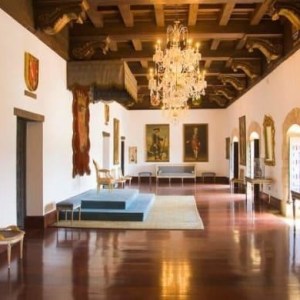 Elegant hall with chandeliers, paintings, and ornate mirrors on wood-trimmed walls.