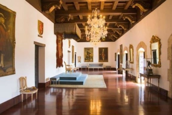 Elegant hall with chandeliers, paintings, and ornate mirrors on wood-trimmed walls.