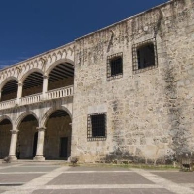 Historic stone building with arches and palm tree against blue sky.