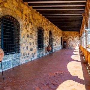 Stone corridor with arches and clay pots, overlooking a view on the right.