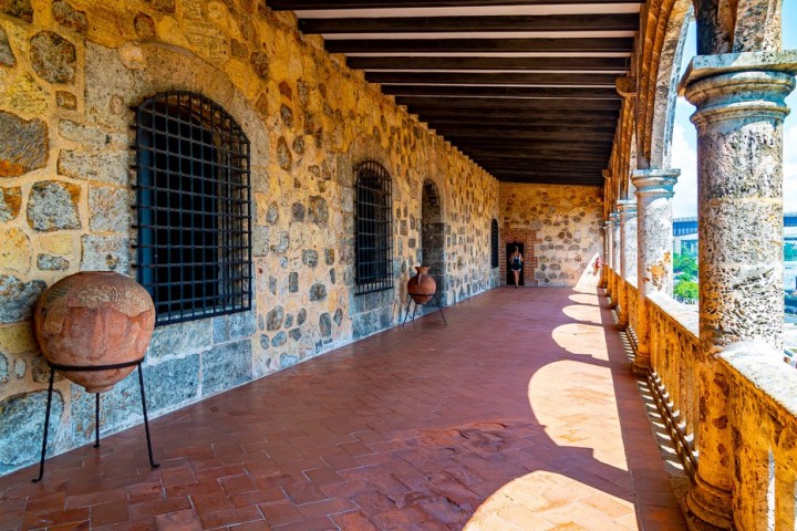 Stone corridor with arches and clay pots, overlooking a view on the right.