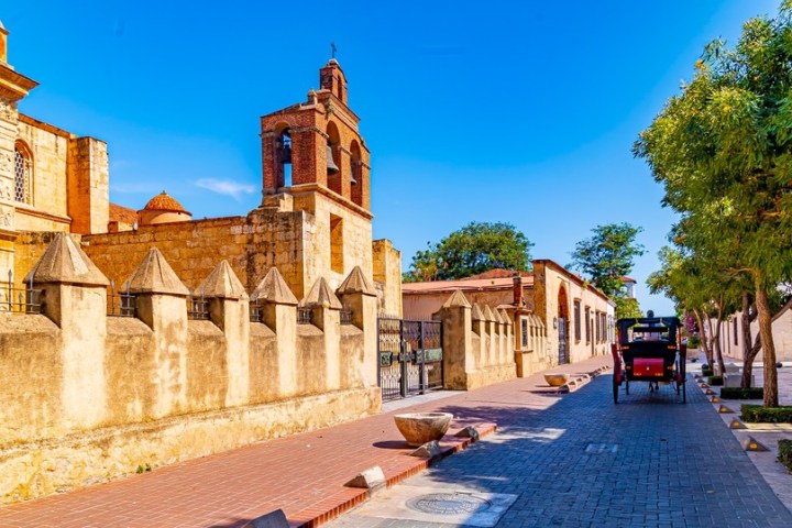 Historic street with trees, a horse-drawn carriage, and an old church building under a clear blue sky.