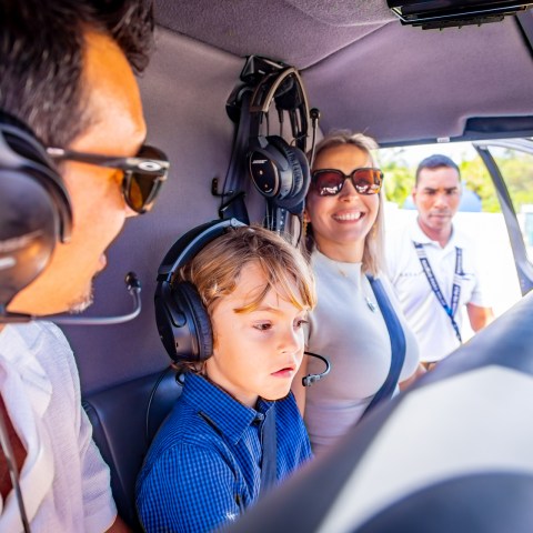 People inside a helicopter wearing headsets, including a child in the front seat.