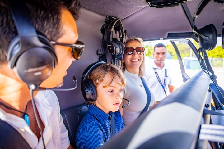 People inside a helicopter wearing headsets, including a child in the front seat.