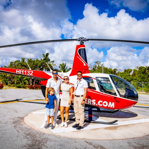 Group of four people in front of a red helicopter on a sunny day.