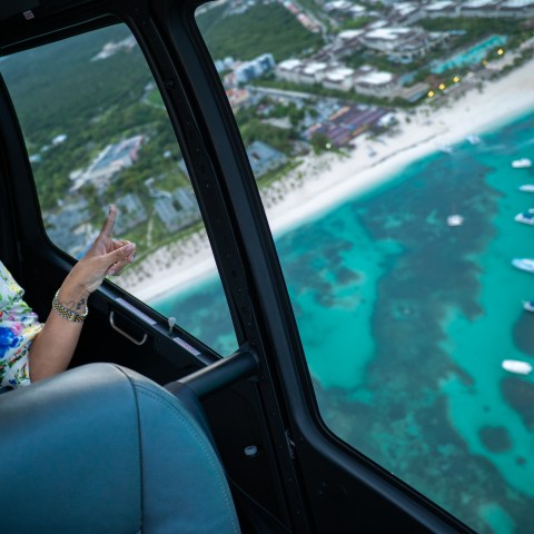 Woman in helicopter looking over coastline with boats and buildings.
