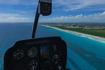 View from helicopter cockpit flying over coastline with blue ocean and sky.