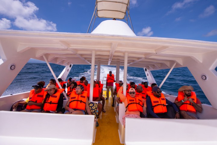 People on a boat wearing orange life jackets under a clear sky.