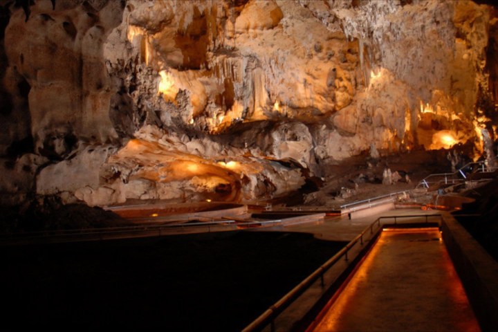 Illuminated cave interior with rock formations and a pathway.
