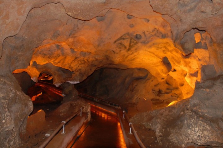 Illuminated cave with rocky walls and a paved pathway with railings.