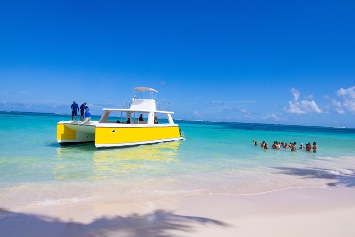 Yellow boat near beach, people swimming in turquoise water under a clear blue sky.