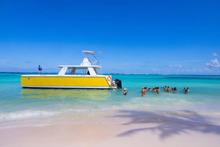 Yellow boat near shore with people swimming in clear blue water under a sunny sky.