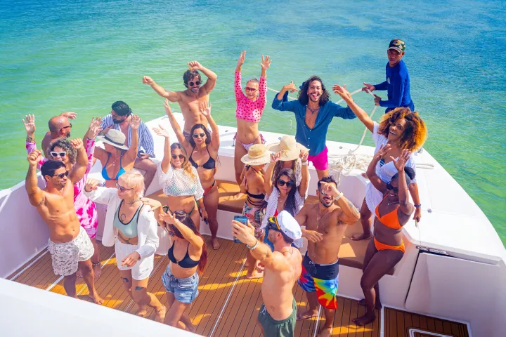 Group of people dancing on a boat in swimwear with the ocean in the background.