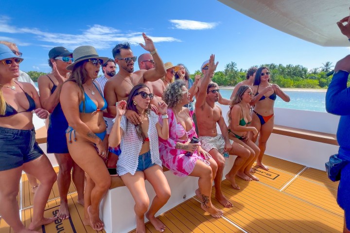 Group of people in swimwear enjoying a party on a boat near an island