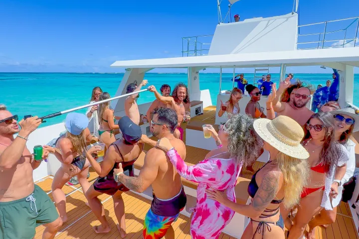 Group of people dancing and celebrating on a boat in clear blue water.