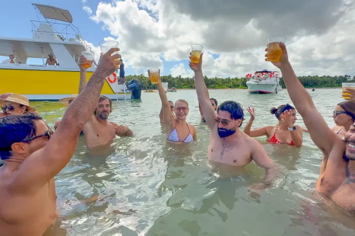 Group of people in water raising cups, with boats in the background.