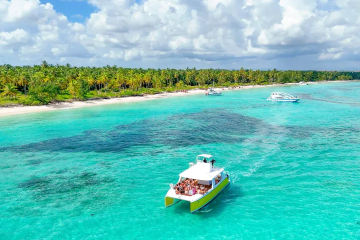 Boat on turquoise water near a tropical beach with palm trees.