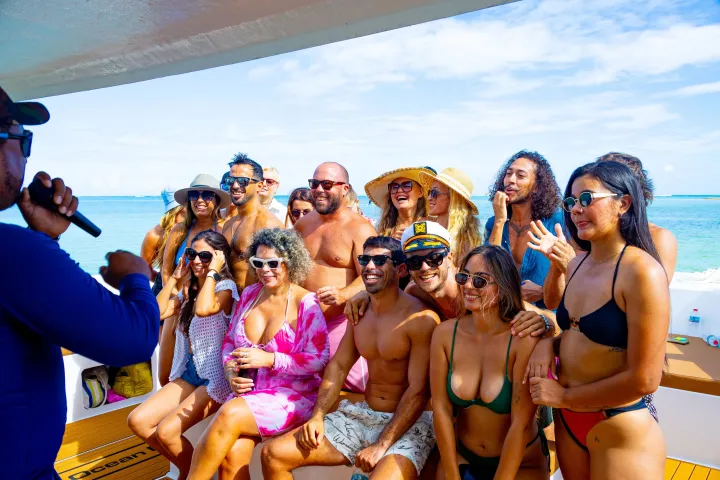 A group of people in swimwear enjoying a sunny day on a boat, with a person singing into a microphone.