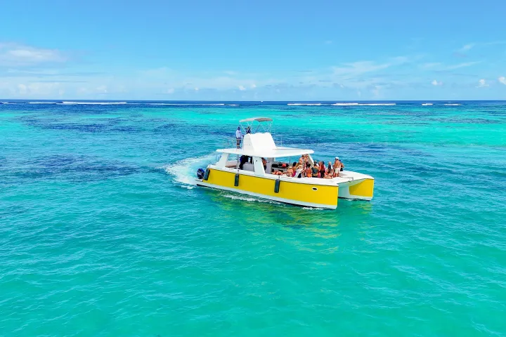 Yellow boat with people cruising on turquoise ocean under clear blue sky.