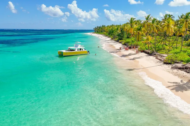 Tropical beach with palm trees, turquoise water, and a yellow boat near the shore under clear blue skies.