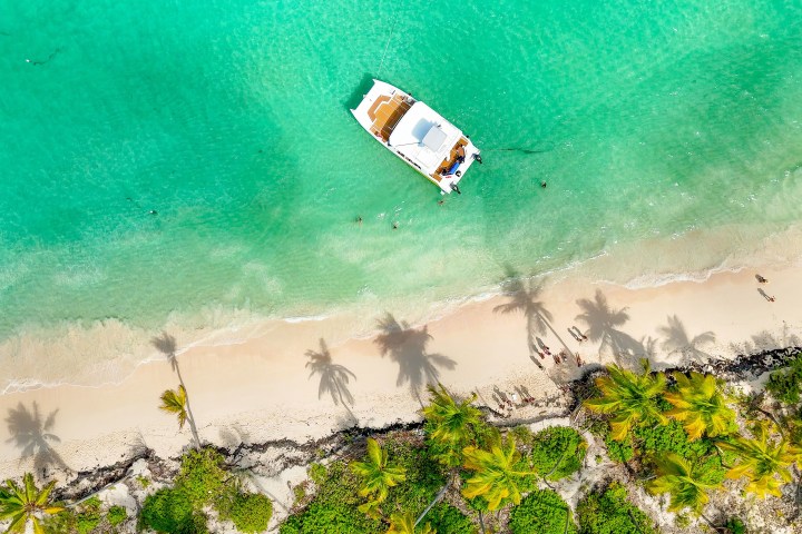 Aerial view of a boat near a tropical beach with palm trees and turquoise water.