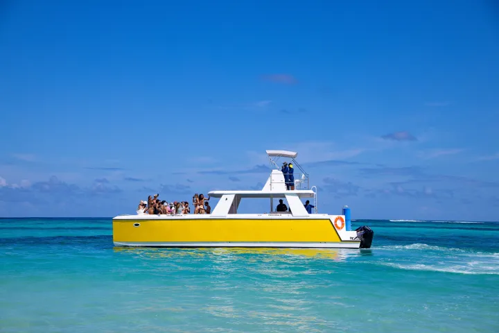 Yellow boat with people on turquoise ocean under clear blue sky.