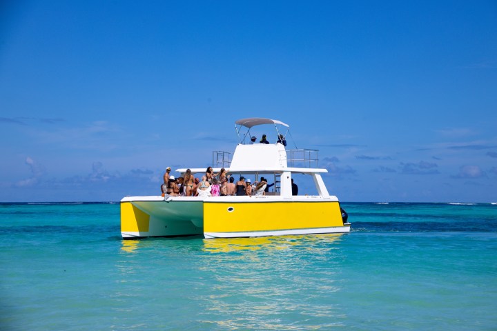People on a yellow catamaran in turquoise waters under a clear blue sky.