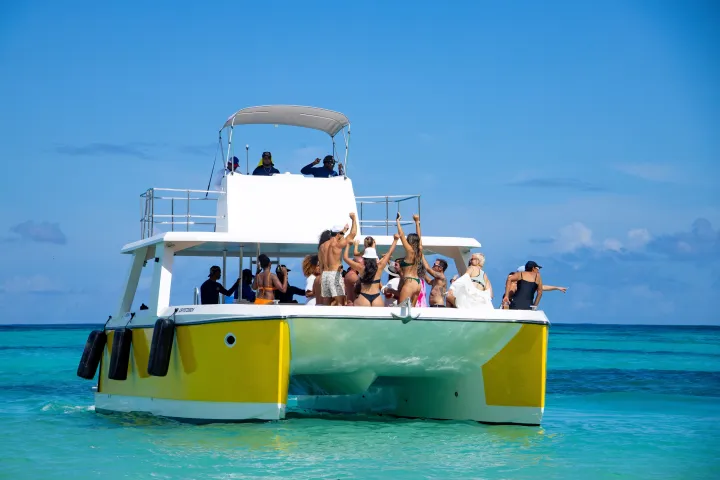 People dancing and relaxing on a white and yellow boat in clear blue ocean water.